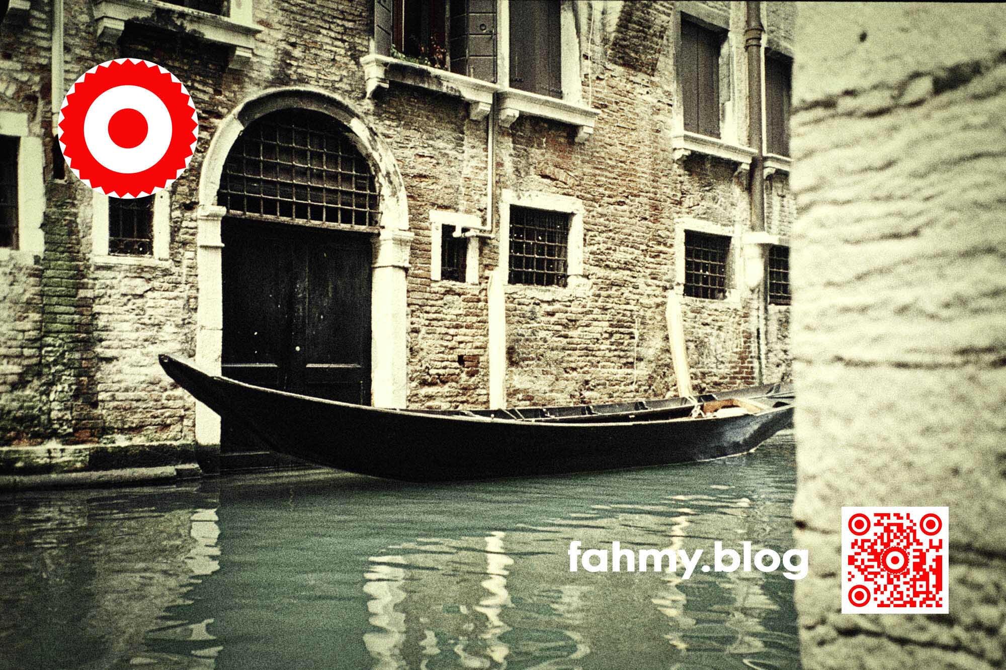 Parkende Gondel - Venedig 2000, (c) 2022 fahmy.blog Typische Straßenszene in Venedig. Eine parkende Gondel. Das rot-weiß-rote Logo von fahmy.blog ist in der linken oberen Ecke, der QR-Code und Bildunterschrift von fahmy.blog ist in der rechten Ecke zu sehen.